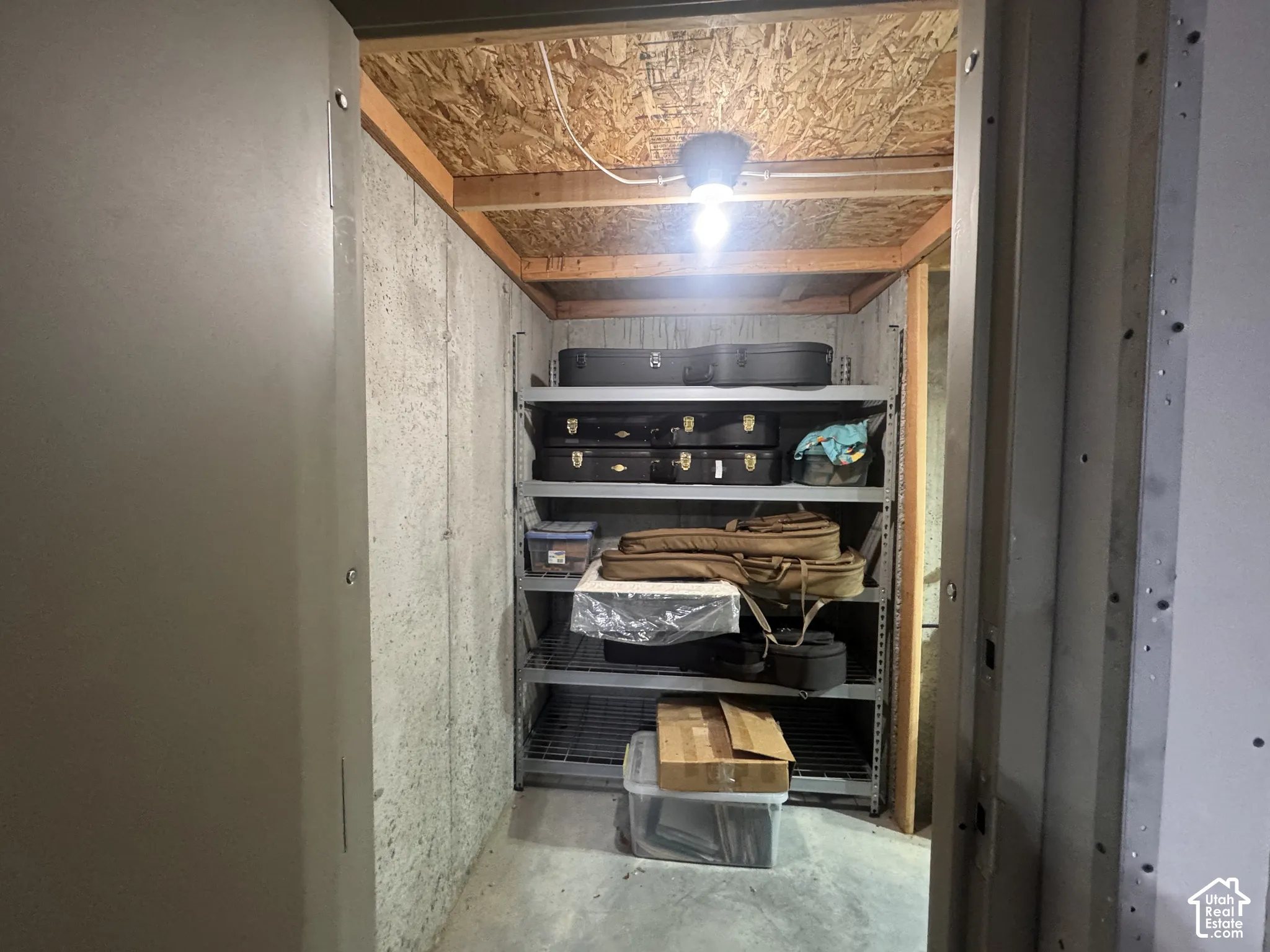 Storage room featuring unfinished concrete walls, exposed wood ceiling joists, concrete flooring, and industrial-grade metal shelving