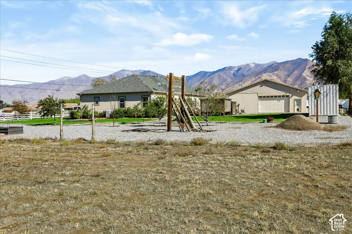 Expansive grounds featuring a gravel lot, detached garage, mountain backdrop, and white rail fencing
