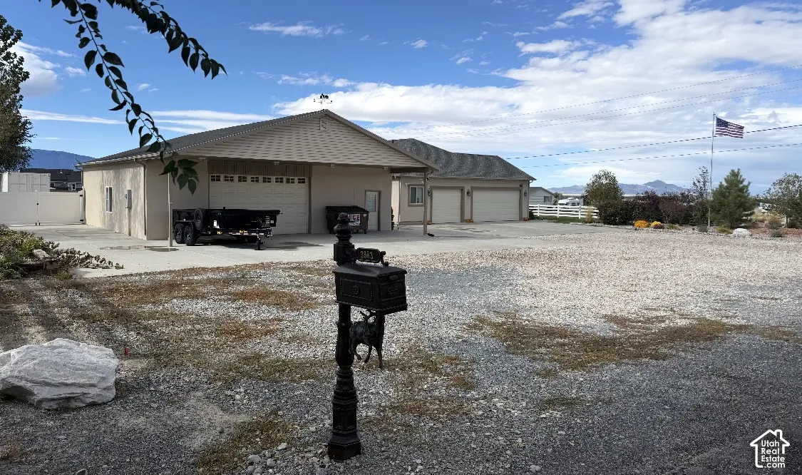 Exterior view featuring a multi-bay garage structure with metal-paneled overhead doors, a covered parking apron, and extensive gravel grounds