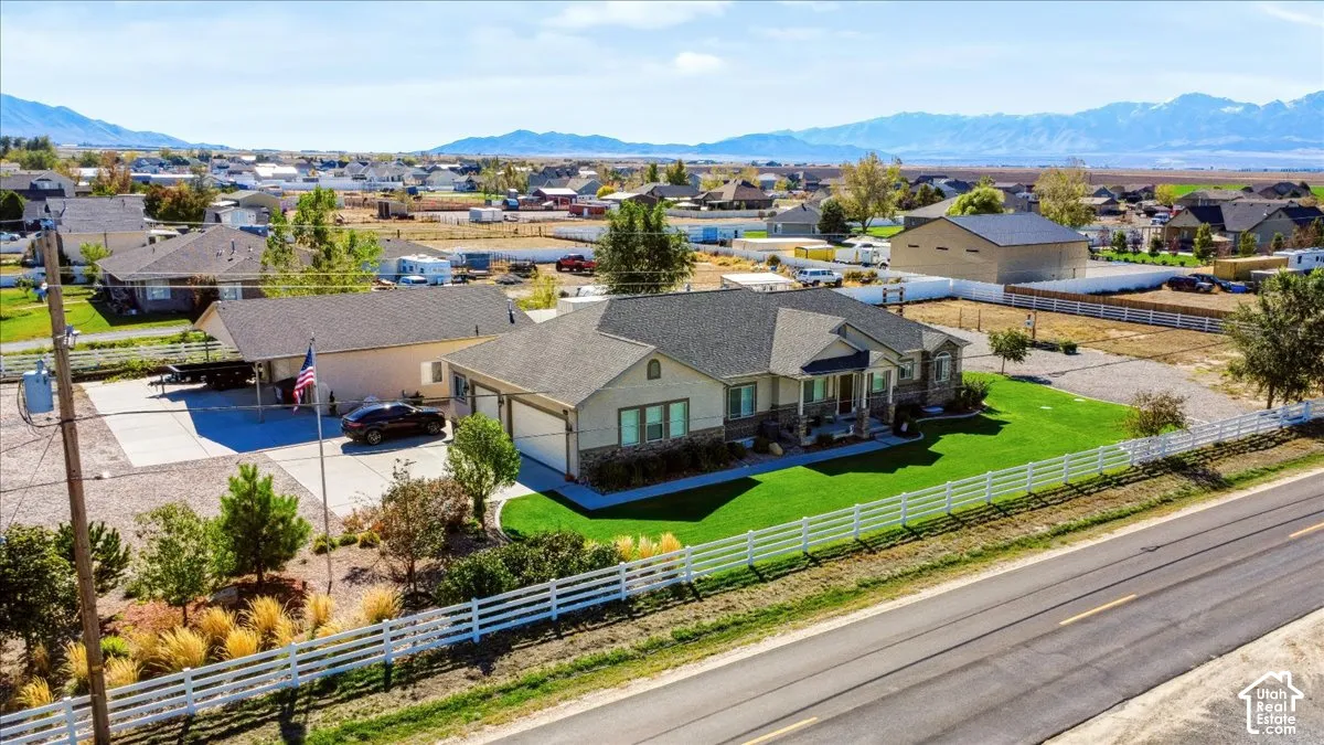 Single-story residence featuring stone and siding exterior, attached multi-car garage, expansive concrete driveway, white perimeter fencing, and mountain backdrop