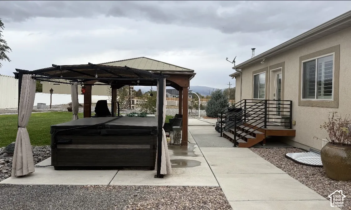 Outdoor living space featuring a covered gazebo, hot tub, concrete patio, and metal railings