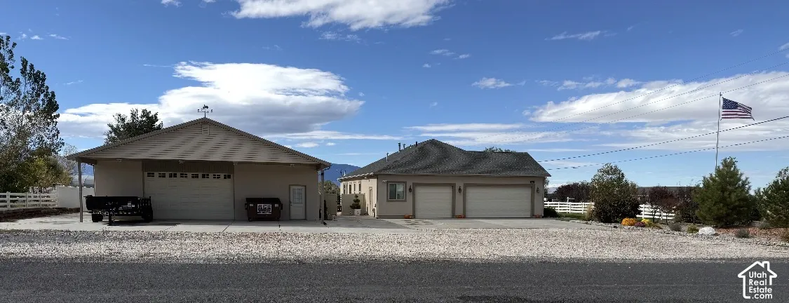 Detached garage with a pitched roof, attached multi-car garage, expansive paved driveway, and white perimeter fencing