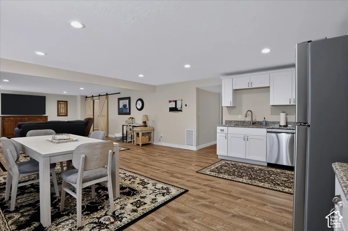 Kitchenette featuring white cabinetry, stone-finish countertops, stainless steel dishwasher, and recessed lighting, all complemented by wood-finish flooring