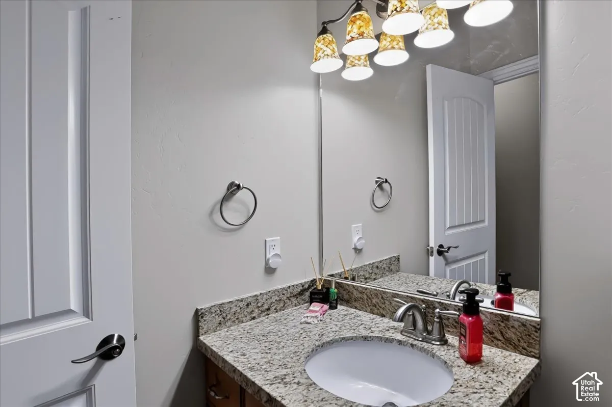 Stone-surface countertop with integrated oval sink, multi-light fixture, full-width vanity mirror, and brushed-metal hardware