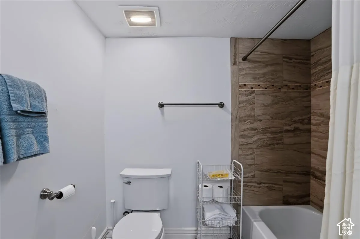 Bathroom featuring a shower-tub combination with horizontal stone-finish tile surround and a decorative glass mosaic accent strip, complemented by a white porcelain toilet and metal hardware