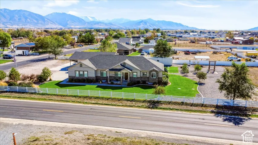 Single-story residence featuring stone and composite siding, shingled roof, white vinyl perimeter fencing, manicured lawn, and mountainous horizon