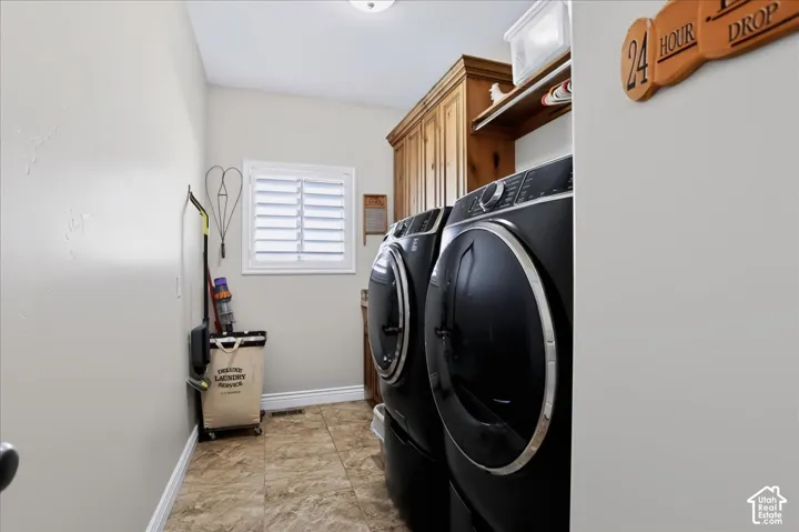 Laundry room featuring custom wood cabinetry, stone-finish tile flooring, and interior window shutters