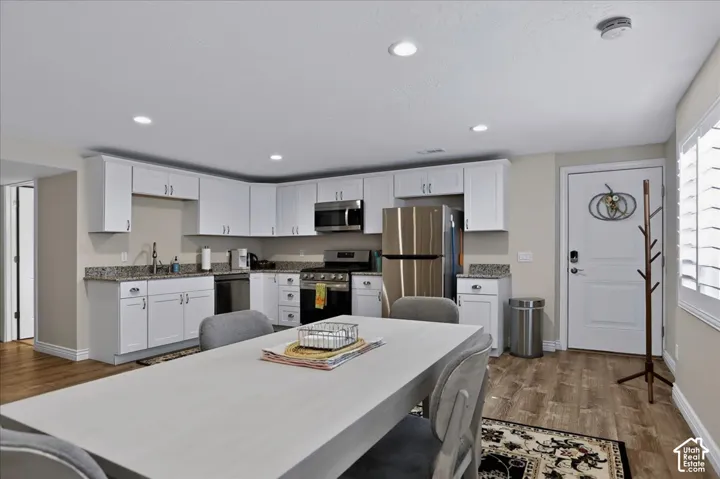 Kitchen featuring white cabinetry, stone-surface countertops, stainless steel appliances, wood-finish flooring, and recessed lighting