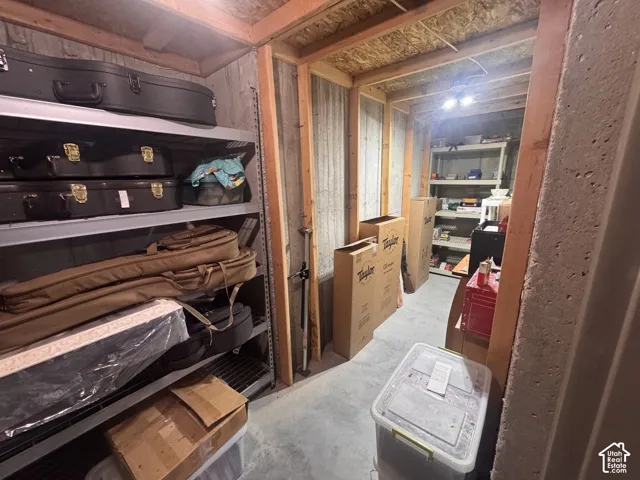 Storage room with exposed wood framing, concrete walls, concrete floor, and built-in metal shelving