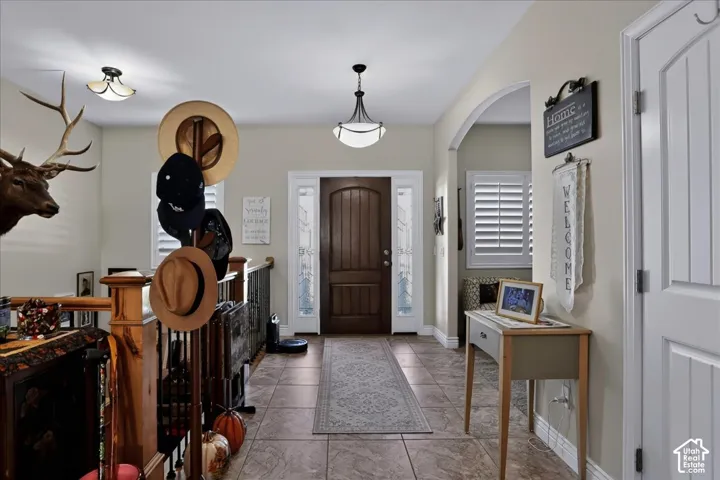 Entryway featuring a dark wood-finish front door with sidelights, tile flooring, arched wall detailing, and dual hanging light fixtures