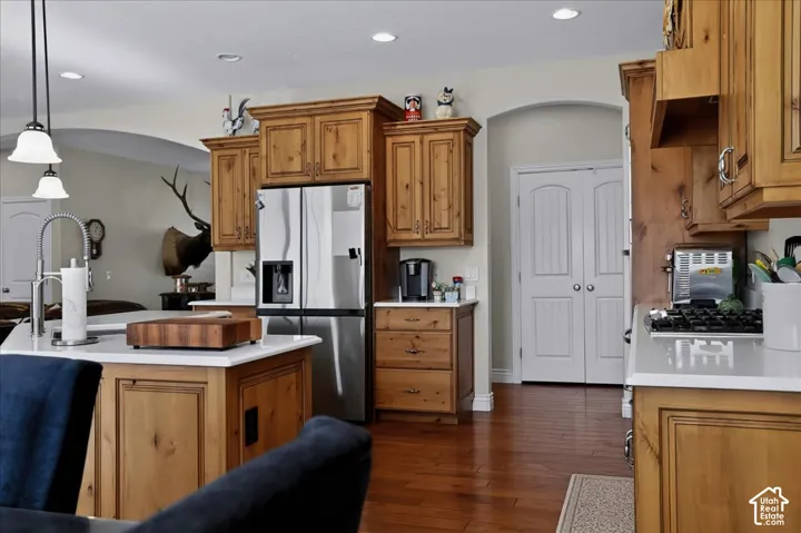 Kitchen featuring custom wood cabinetry, a central island with a solid surface countertop, wood-finish flooring, stainless steel appliances, and recessed lighting