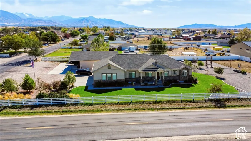 Single-story residence with a stone and siding exterior, asphalt shingle roof, manicured lawn, white rail fencing, and mountain backdrop