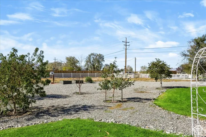 Expansive grounds featuring gravel landscaping, mature trees, a white ranch-style perimeter fence, manicured lawn sections, and a white metal garden arch