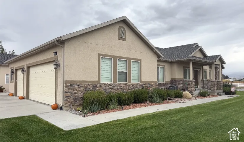 Stucco and stacked stone exterior featuring a three-car garage, covered entryway, and asphalt shingle roofing