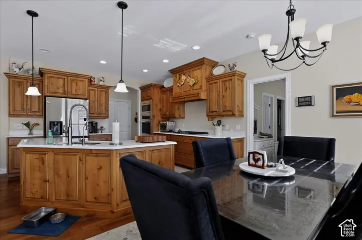 Kitchen featuring knotty wood cabinetry, light-toned countertops, a center island with a stainless steel sink, built-in double wall ovens, and pendant and chandelier lighting