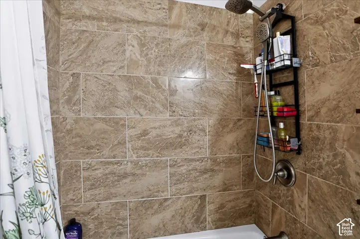 Shower featuring large-format rectangular stone-finish wall tile, a metallic multi-function handheld shower head, and a single-handle pressure-balance control valve