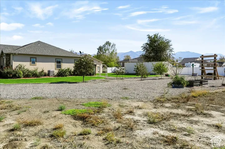 Expansive backyard featuring a gravel area, manicured lawn sections, mature trees, mountain backdrop, and perimeter white vinyl fencing