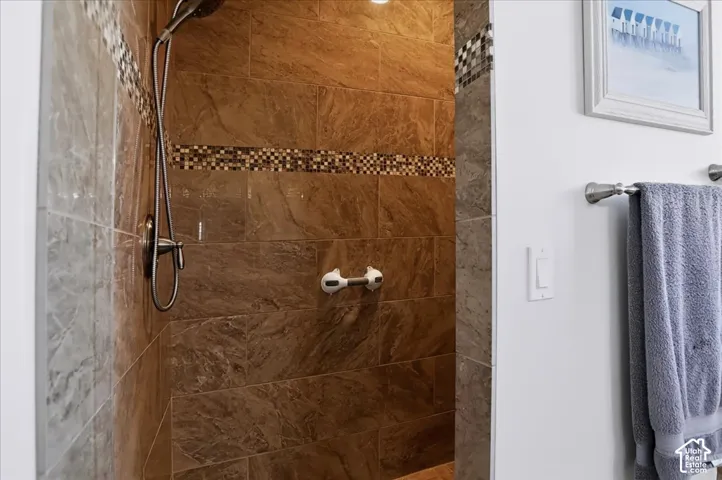 Walk-in shower featuring brown stone-style tile, a decorative mosaic tile accent border, and a wall-mounted brushed-finish shower head