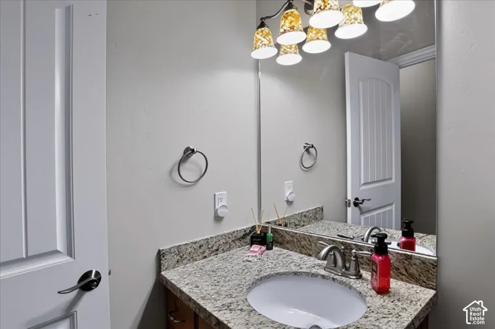 Stone-surface countertop with integrated oval sink, multi-light fixture, full-width vanity mirror, and brushed-metal hardware