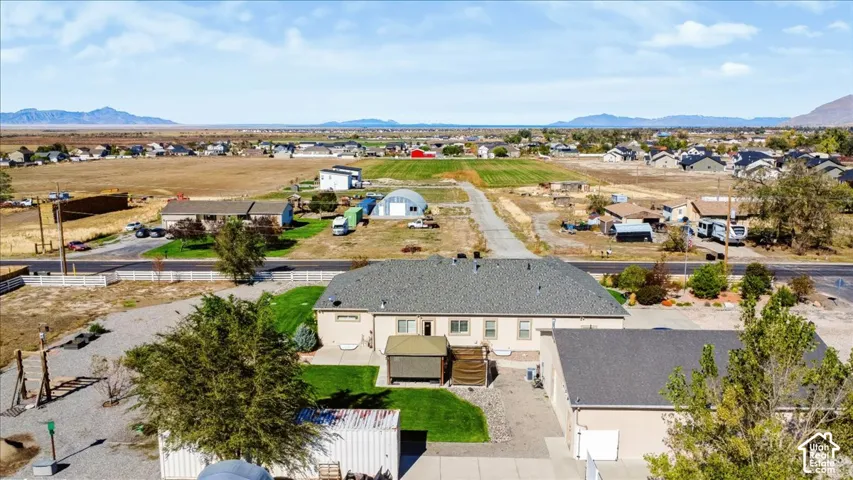 Aerial perspective featuring a single-story residence with a multi-car garage, manicured lawn, paved driveway, and mountain backdrop