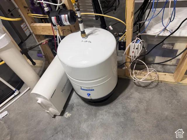 Water filtration system featuring a vertical white storage tank, pump, and white cylindrical canister unit mounted on concrete flooring