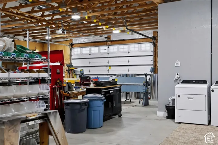 Multi-bay garage featuring exposed timber ceiling trusses, a sectional overhead door with glass inserts, concrete flooring, and laundry hookups