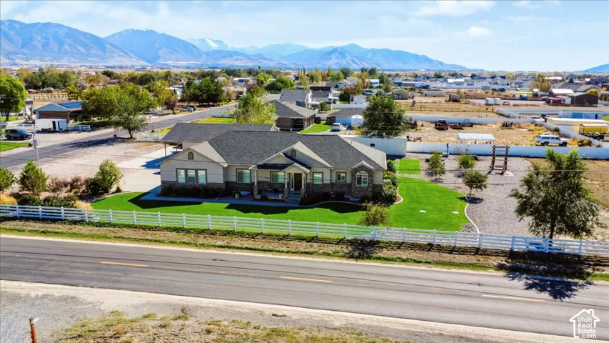 Single-level residence with stone and horizontal siding exterior, asphalt shingle roof, white rail fencing, manicured lawn, and mountain backdrop