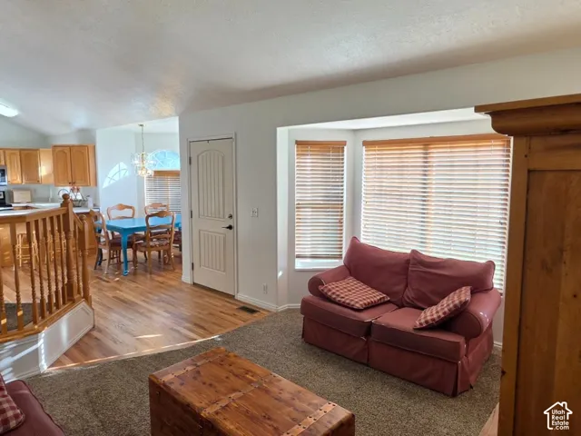 Carpeted living area with bay windows and wood-finish blinds, staircase with wood railing, and wood-finish flooring extending into the kitchen and dining area