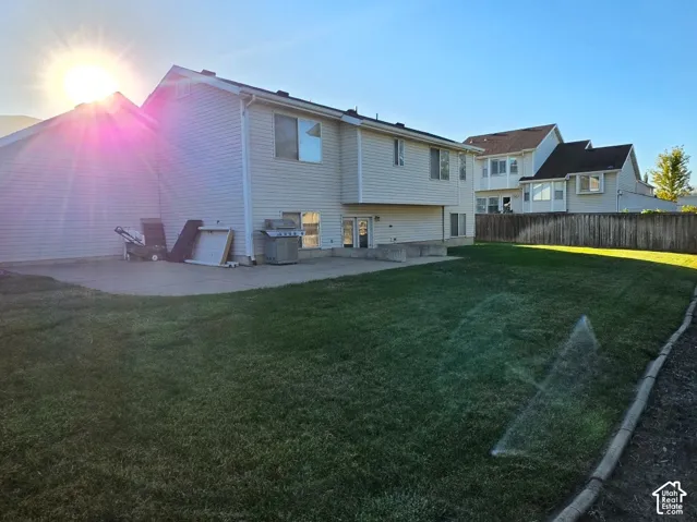 Expansive backyard with a large concrete patio, manicured lawn, and a privacy fence