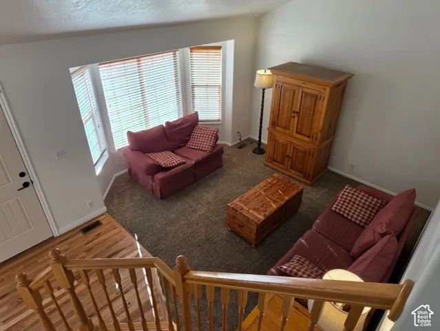 Bay window with blinds, vaulted ceiling, wood-finish flooring, and wood banister