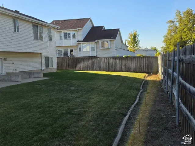 Expansive grassy yard with a wooden privacy fence, concrete patio, and exterior siding