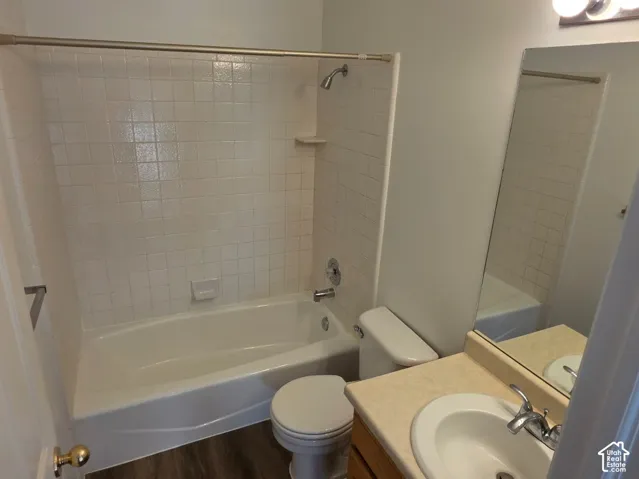 Bathtub with white tile surround, vanity with integrated sink, mirror, and overhead lighting fixture