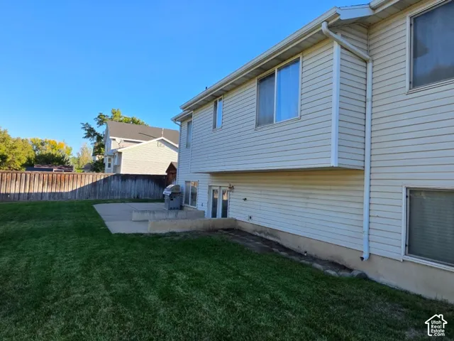Expansive grassy area with a wooden privacy fence, concrete patio, and a walk-out lower level