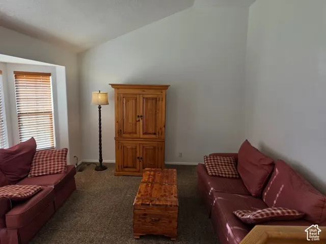 Vaulted ceilings, bay window with blinds, carpeted flooring, and light-toned walls