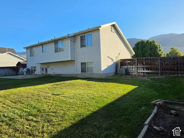 Expansive backyard with a manicured lawn, full privacy fencing, a concrete patio, and a raised garden bed