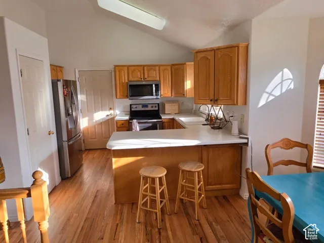 Vaulted ceiling, wood-finish flooring, light wood cabinetry, stainless steel appliances, and an arched window