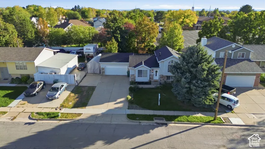 Aerial perspective of a detached residential property featuring a concrete driveway, two-car garage, stone and siding exterior, and mature evergreen landscaping