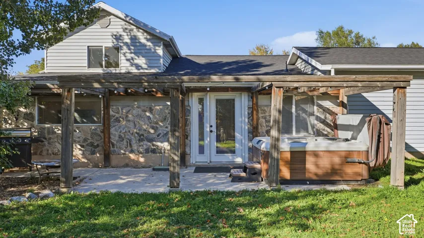 Rear exterior featuring a concrete patio, wood pergola, stone-veneer siding, and an integrated hot tub