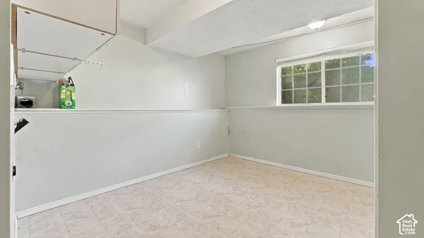 laundry roomInterior space featuring light-toned tile flooring, built-in upper cabinetry, a sliding window with horizontal blinds, and a neutral wall finish