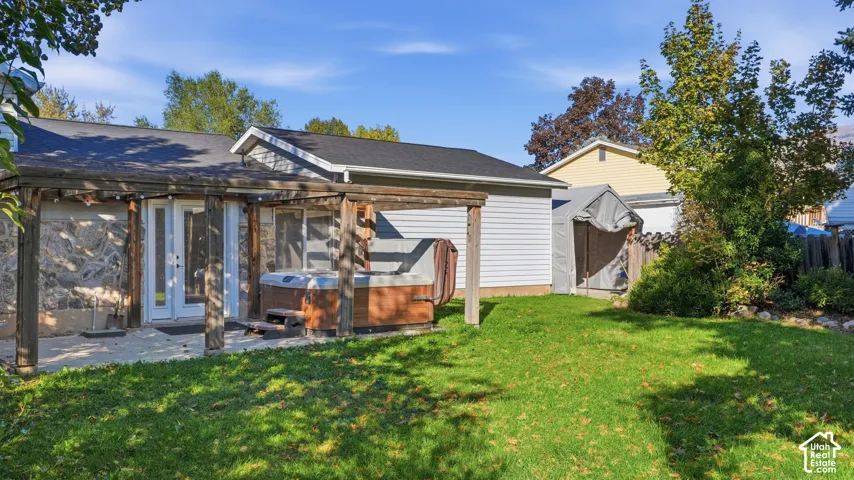 Backyard featuring a paved patio with a wood-beam pergola, integrated hot tub, and established lawn