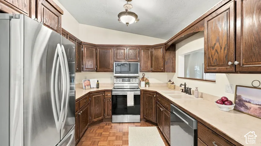 Kitchen featuring dark wood cabinetry, stainless steel appliances, solid surface countertops, a double-basin sink, and parquet flooring