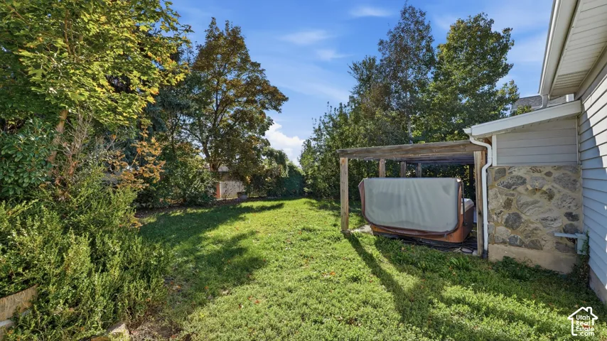 Rear exterior featuring a covered patio, stone veneer siding, mature trees, and an open lawn area