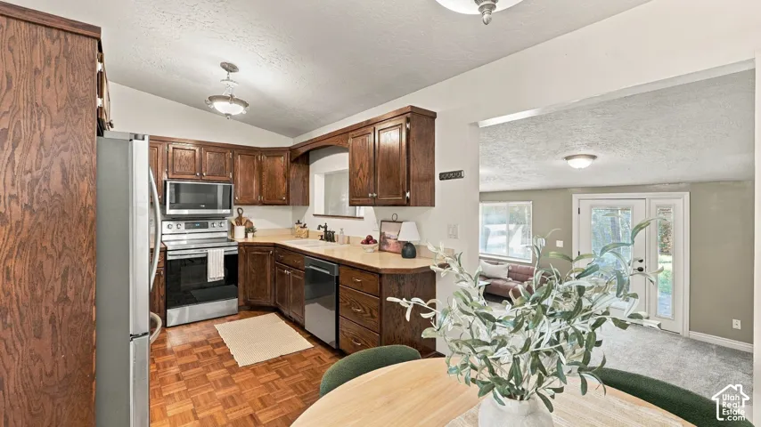 Kitchen featuring stained wood cabinetry, stainless steel appliances, solid surface countertops, and parquet wood-finish flooring