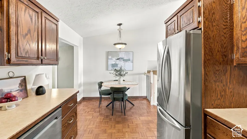 Kitchen featuring custom wood cabinetry, stainless steel refrigerator, parquet wood-finish flooring, vaulted ceiling, and an integrated pendant light fixture