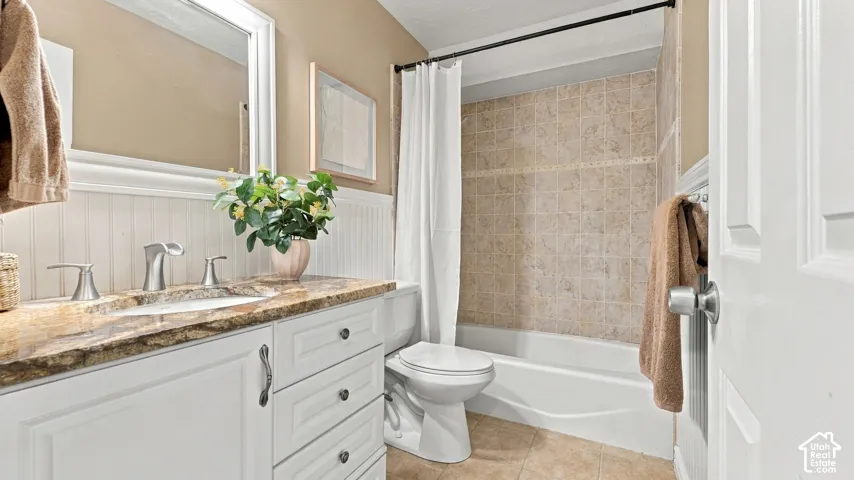 Bathroom featuring a stone-surface vanity countertop, white cabinetry with integrated drawers, beadboard wainscoting, and a tiled shower surround