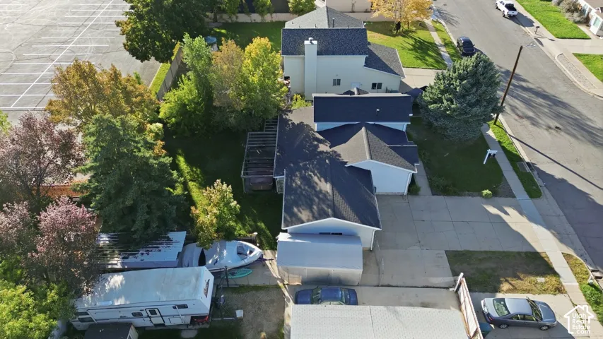 Aerial view of property featuring a multi-pitched shingled roof, paved driveway, detached covered carport, and mature trees on the lot