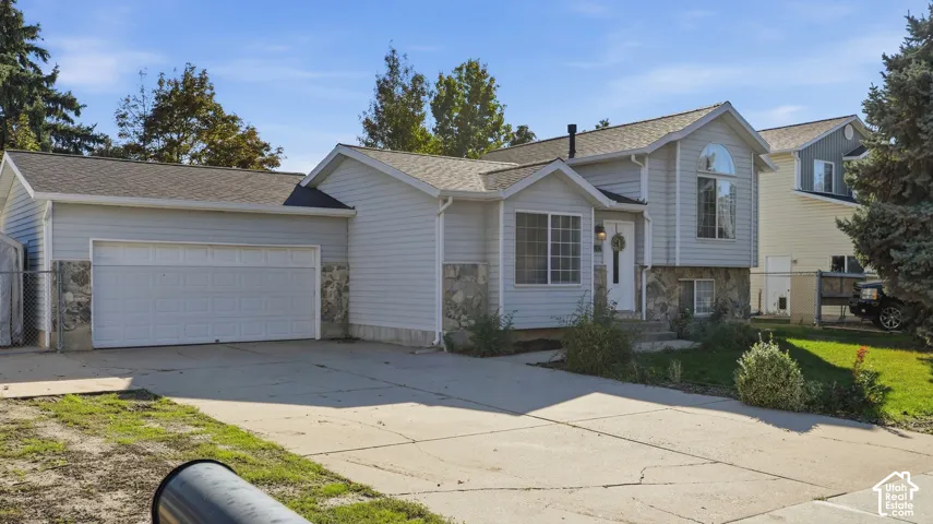 Split-level exterior featuring light gray horizontal siding, stone veneer accents, a multi-gabled roofline, an attached two-car garage, and a concrete driveway