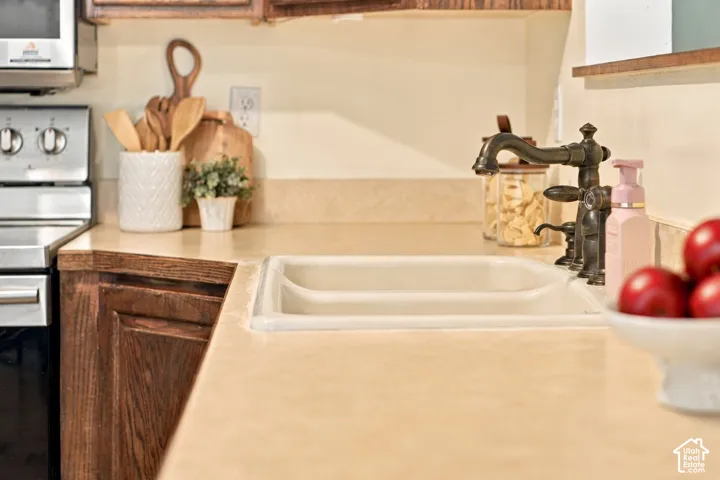 Kitchen featuring solid-surface countertops, dual-basin undermount sink, antiqued bronze-finish faucet, and stained wood cabinetry