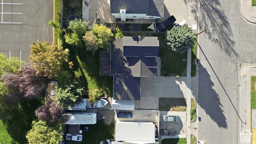 Aerial perspective featuring a residential lot with a paved driveway, mature trees, multi-pitched roofline, and grass lawn