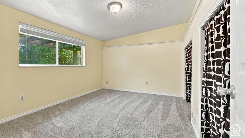 Room featuring neutral wall tones, wall-to-wall carpeting, a horizontal sliding window with a window covering, a vaulted ceiling, and dual doorways